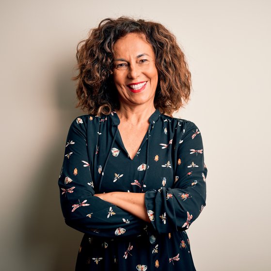 Lockige Frau lacht in die Kamera, trägt eine schwarzer Bluse, auf der Schmetterlinge und Insekten abgedruckt sind