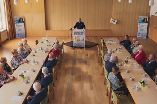 Infoveranstaltung Prävention Polizeibeamter am Rednerpult. Links und rechts davon Roll up Ortsverein Untergruppenbach. Vordergrund zwei Tischreihen mit zhörenden.