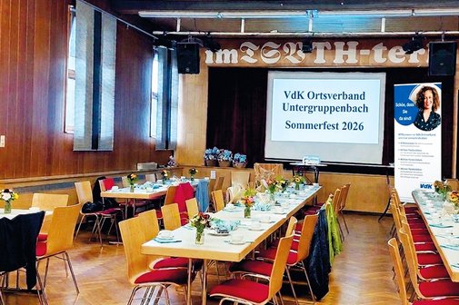 Sommerfest 2026 Ansicht auf noch leeren aber schon dekorierten Saal. Lage Tischreihen im Hintergrund Leinwand mit Mit Text und rechts Roll up des Ortsverbandes